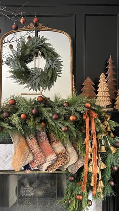 a mantle decorated for christmas with stockings and wreaths on it, along with other holiday decorations