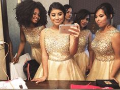 four women in gold dresses are taking a selfie with their cell phone while looking into the mirror