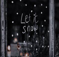 the words let it snow written on a glass window with candles in front of it