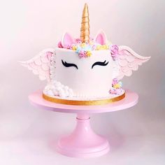 a white cake with pink icing and gold trimmings has a unicorn horn on top