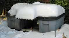 two trash cans covered in snow next to bushes