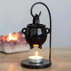 a black tea light holder with a lit candle in it on a wooden table next to a fire