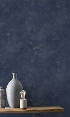 two white vases sitting on top of a wooden shelf next to a blue wall