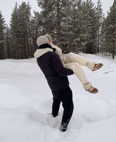 a man holding onto another person in the snow with trees in the back ground behind him