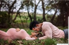 a man and woman laying on the grass in front of trees with their heads touching each other