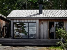 a man standing in the doorway of a small wooden cabin with glass doors and shingled roof