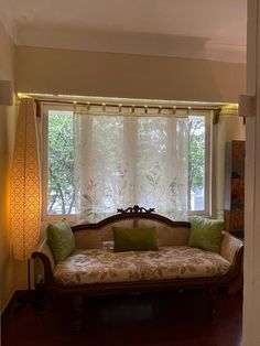 a couch sitting in front of a window next to a wooden table with two green pillows on it