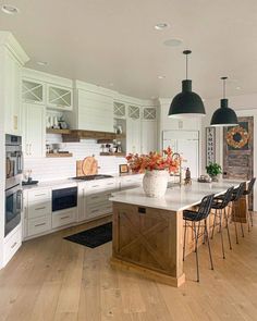 a large kitchen with white cabinets and wooden flooring is pictured in this image, there are several chairs around the island