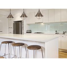 a white kitchen with three stools next to an island