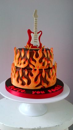 a red and orange cake with a guitar on top is sitting on a white pedestal