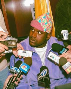 a man sitting in front of microphones surrounded by reporters