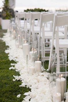 rows of white chairs lined up with flowers and candles on the grass in front of them