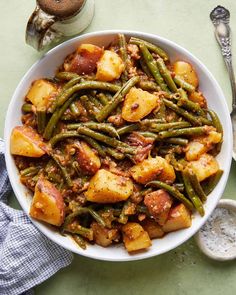 a bowl filled with green beans and potatoes on top of a table next to spoons