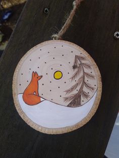 a painted wooden plate with a fox sitting on the ground next to a pine tree