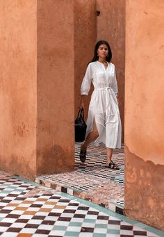 a woman in a white dress is walking through an open doorway with a black handbag