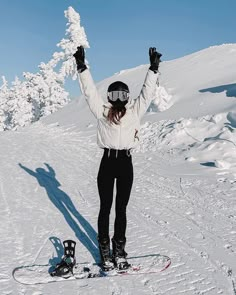 a woman standing on top of a snow covered slope holding her arms in the air