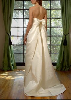 a woman in a white wedding dress looking out the window with her back to the camera