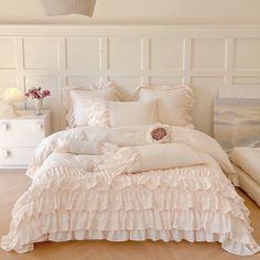 a white bed with ruffles and pillows on top of it in a bedroom