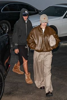 two people walking down the street in front of parked cars and one is wearing a brown leather jacket