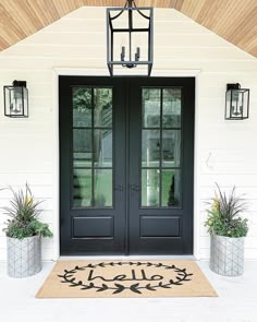 a black double door with two potted plants on the front porch and one light hanging over it