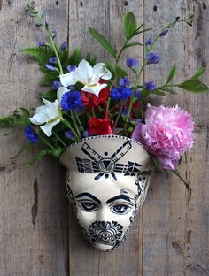 a white mask with flowers in it sitting on a wooden wall