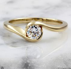 a yellow gold ring with a round diamond in the center on a marble surface,