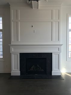 an empty living room with a fireplace and white paneling on the wall above it