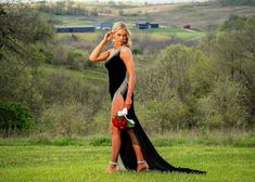 a woman in a long black dress is standing on the grass with her legs crossed