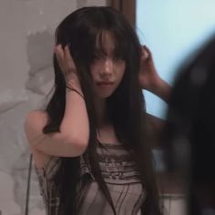 a woman with long black hair standing in front of a mirror holding her hands to her head