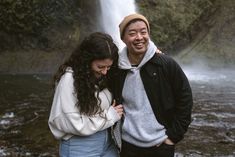 two people standing in front of a waterfall and smiling at the camera with their arms around each other