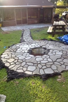 a fire pit in the middle of a yard with grass around it and a picnic table behind it