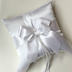 a white pillow with a bow and pearls on the side is laying on a table