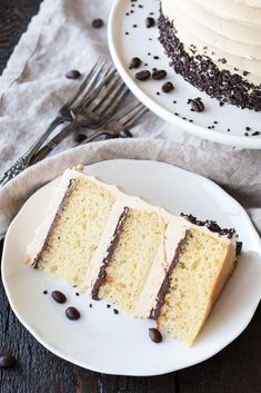 a slice of cake with white frosting and chocolate chips on the side sitting on a plate