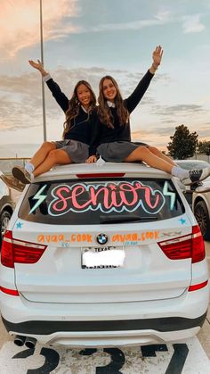 two women sitting on the back of a car with their arms up in the air