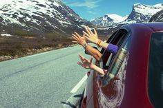 two people waving out the window of a car on a road with mountains in the background