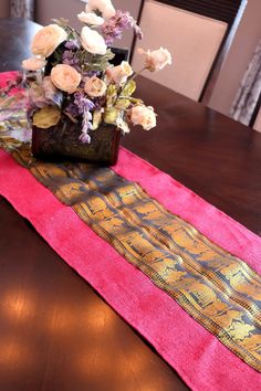 a wooden table topped with a vase filled with flowers on top of a pink runner