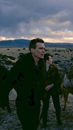 two men and a woman are walking in the desert with their horses on a cloudy day