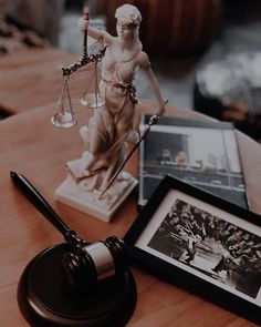 a statue of lady justice sitting on top of a wooden table next to a framed photo