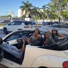 three women sitting in the back of a white convertible car waving at someone with their hand up