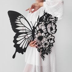 a woman is holding a butterfly cutout in her right hand and wearing a white dress