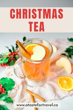 a cup of tea with cinnamon and orange slices in it, surrounded by holly leaves