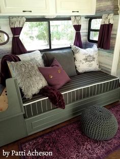 a couch in front of a window with purple curtains and pillows on the windowsill