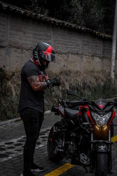 a man with tattoos on his arm standing next to a parked motorcycle and wearing a helmet