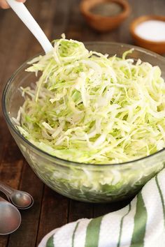 shredded cabbage in a glass bowl with two spoons next to it on a wooden table