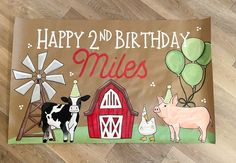 a happy 2nd birthday sign with farm animals and balloons on it's side, in front of a wooden floor