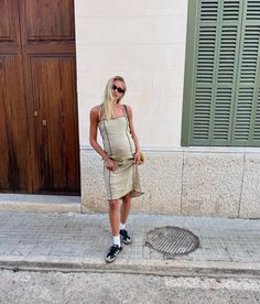 a pregnant woman standing on the sidewalk in front of a building wearing sunglasses and a tan dress