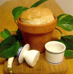 a potted plant sitting next to two cups on top of a wooden table with bread in it