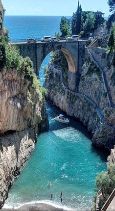 people are swimming in the blue water under an old stone bridge that is built on top of a cliff