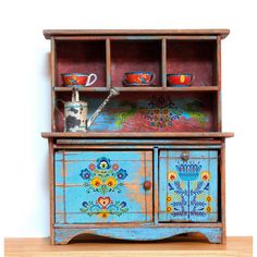 an old wooden cabinet painted with flowers and teapots on the top, sitting on a shelf