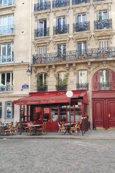 an empty street with tables and chairs in front of a tall building that has balconies on the windows